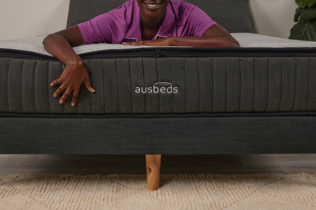Model smiling, hand over the mattress showing ausbeds logo